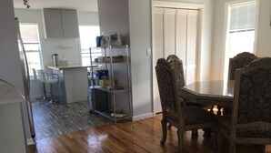 A dining area with a wooden table and chairs, a kitchen in the background, and a shelving unit with various items. - Unique & spacious house with boat docks in Tuckerton beach, NJ (Tuckerton)
