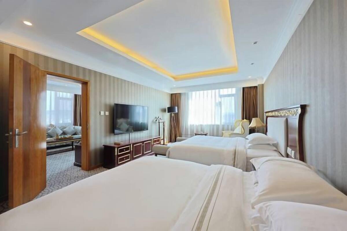 A hotel room with two beds, a TV, a desk, and a sofa.