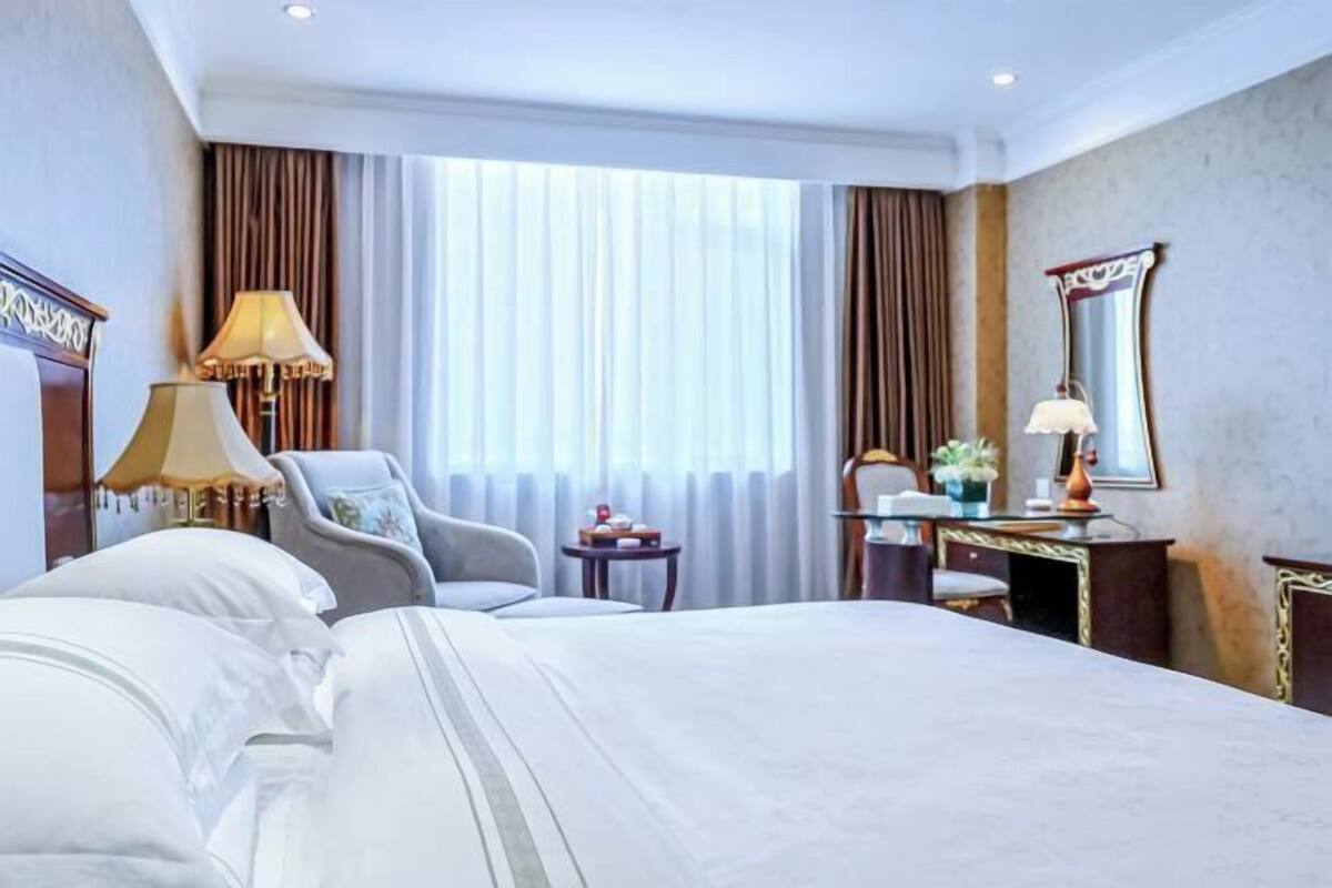A hotel room with a large bed, a desk, a chair, and a window with curtains.