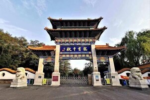Una puerta tradicional china con un letrero azul, flanqueada por estatuas de leones, que da acceso a un edificio con tejado de tejas.