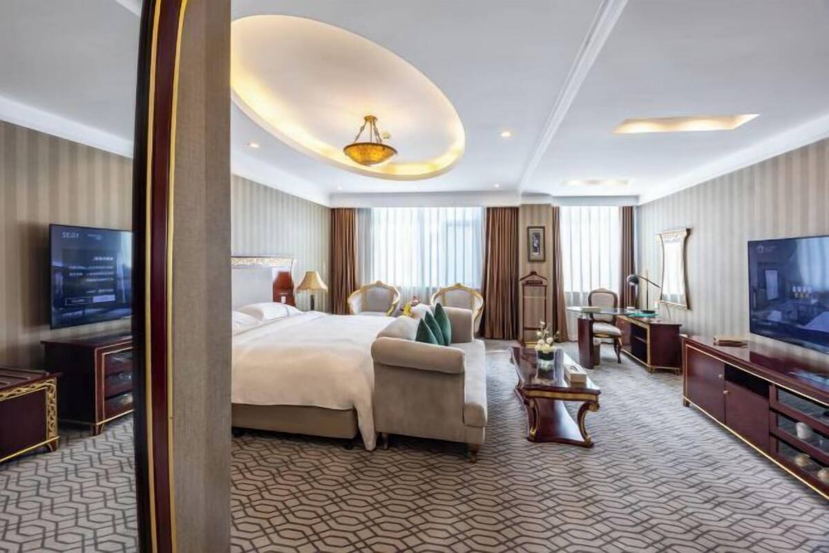 A hotel room with a large bed, a desk, a TV, and a chandelier.
