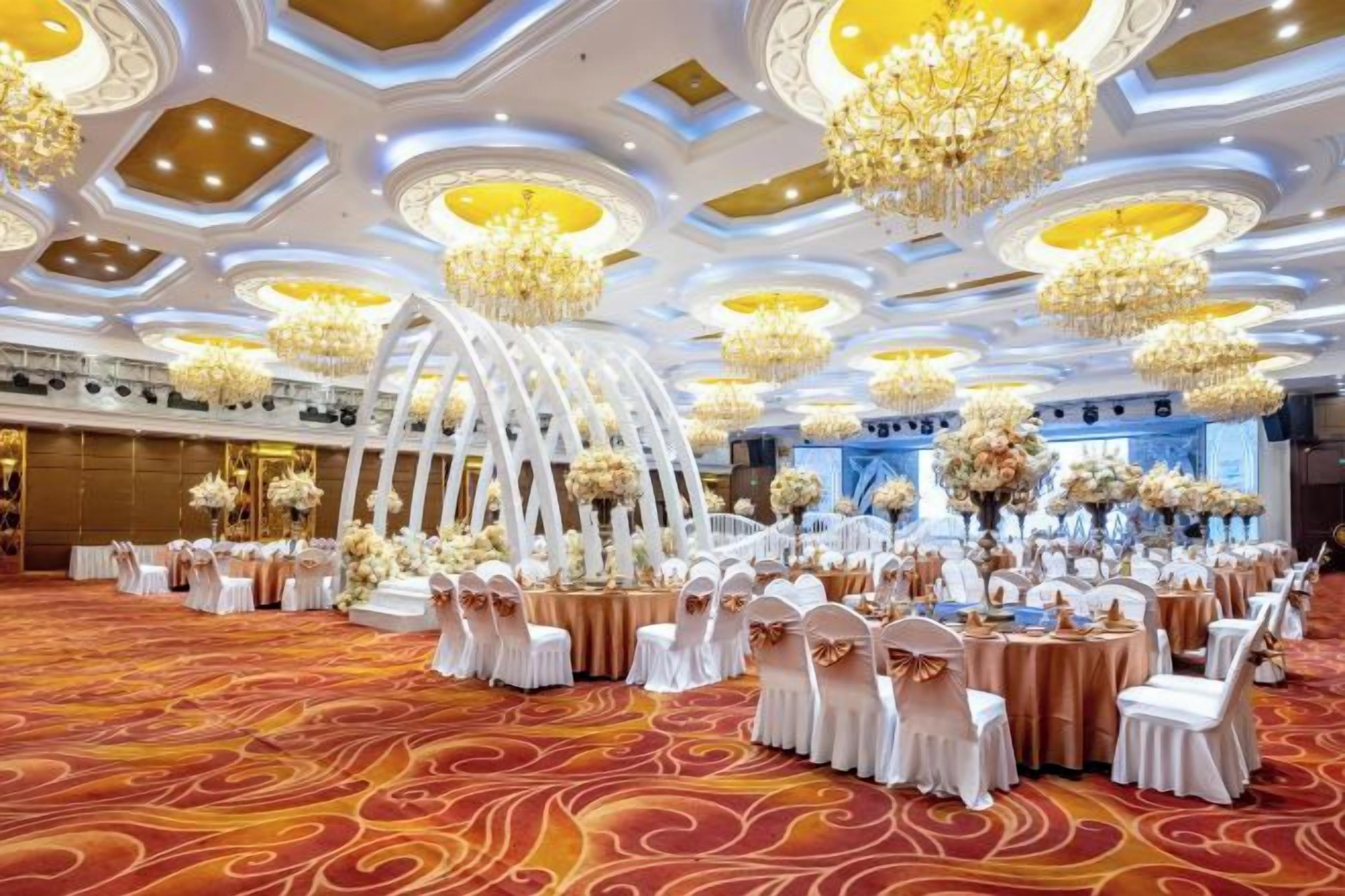 A banquet hall with round tables, white chairs, and floral centerpieces.