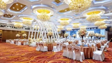A banquet hall with round tables, white chairs, and floral centerpieces.