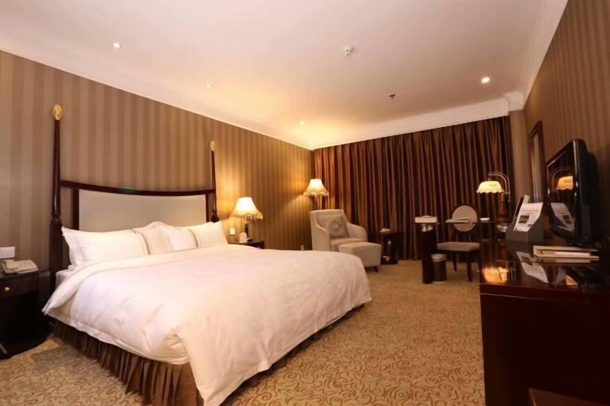 A hotel room with a large bed, two bedside tables with lamps, a chair, a desk with a computer, and a mirror.