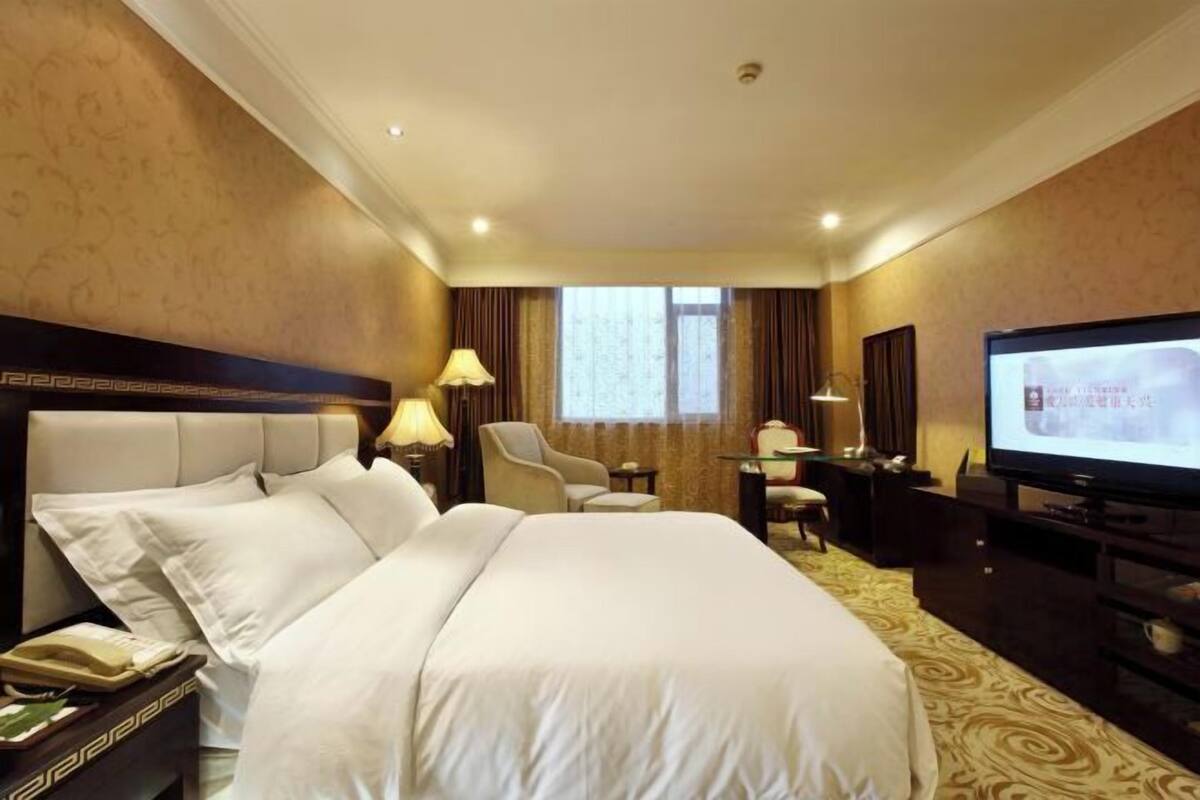 A hotel room with a large bed, a desk with a chair, a television, and a window with curtains.
