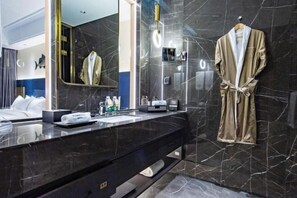 Um banheiro moderno com bancada de mármore preto, um espelho grande e um roupão pendurado na parede.