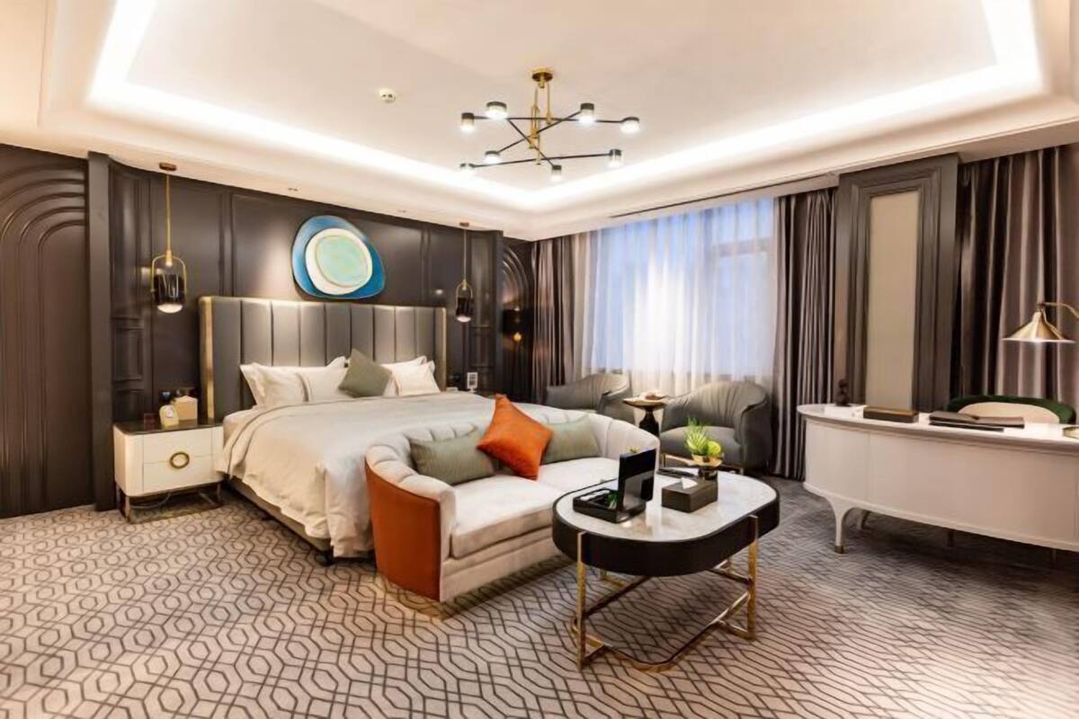 A modern hotel room with a large bed, a round coffee table, a desk, and a large mirror.