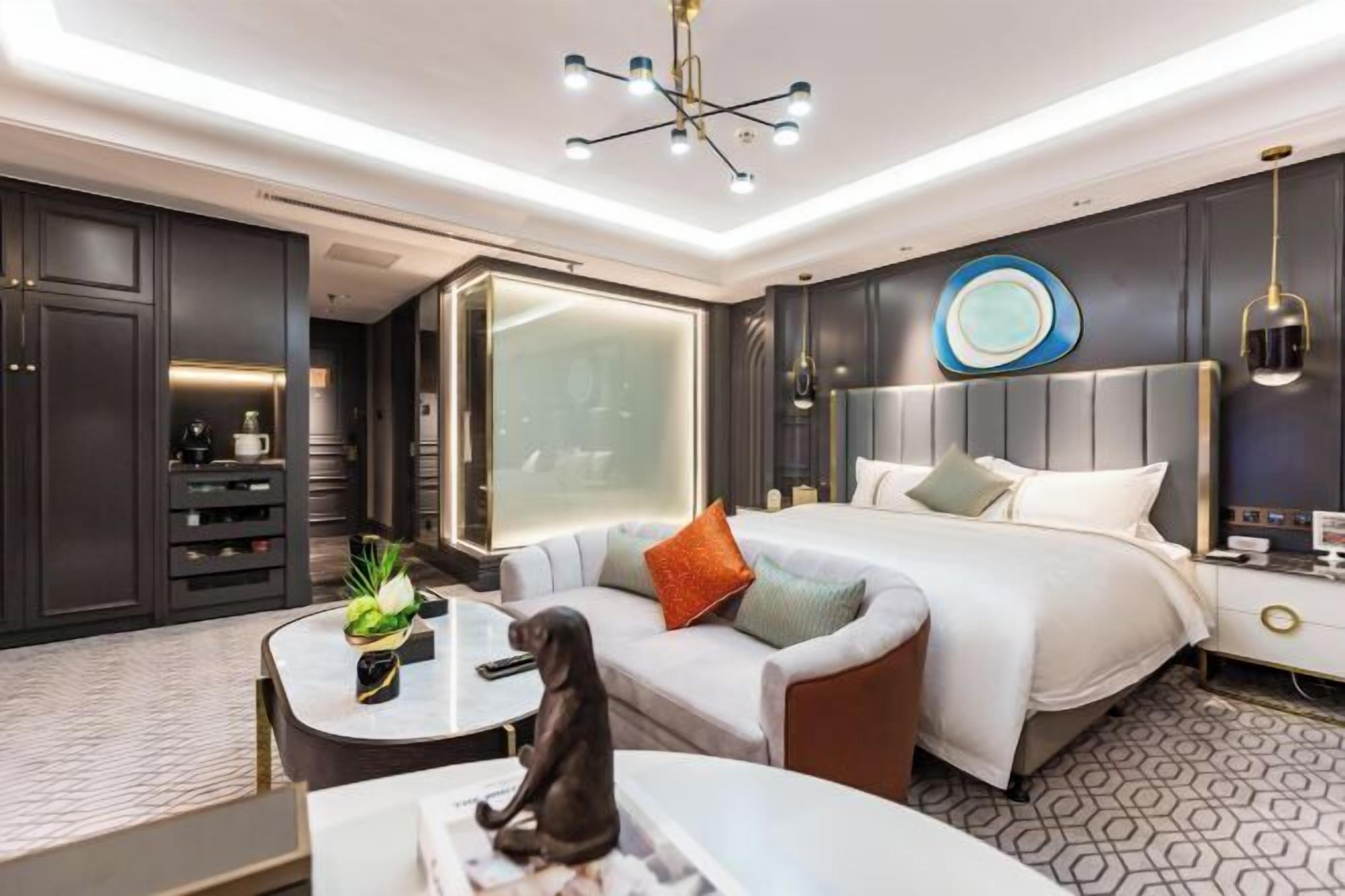 A modern hotel room with a large bed, a sofa, a desk, and a nightstand.
