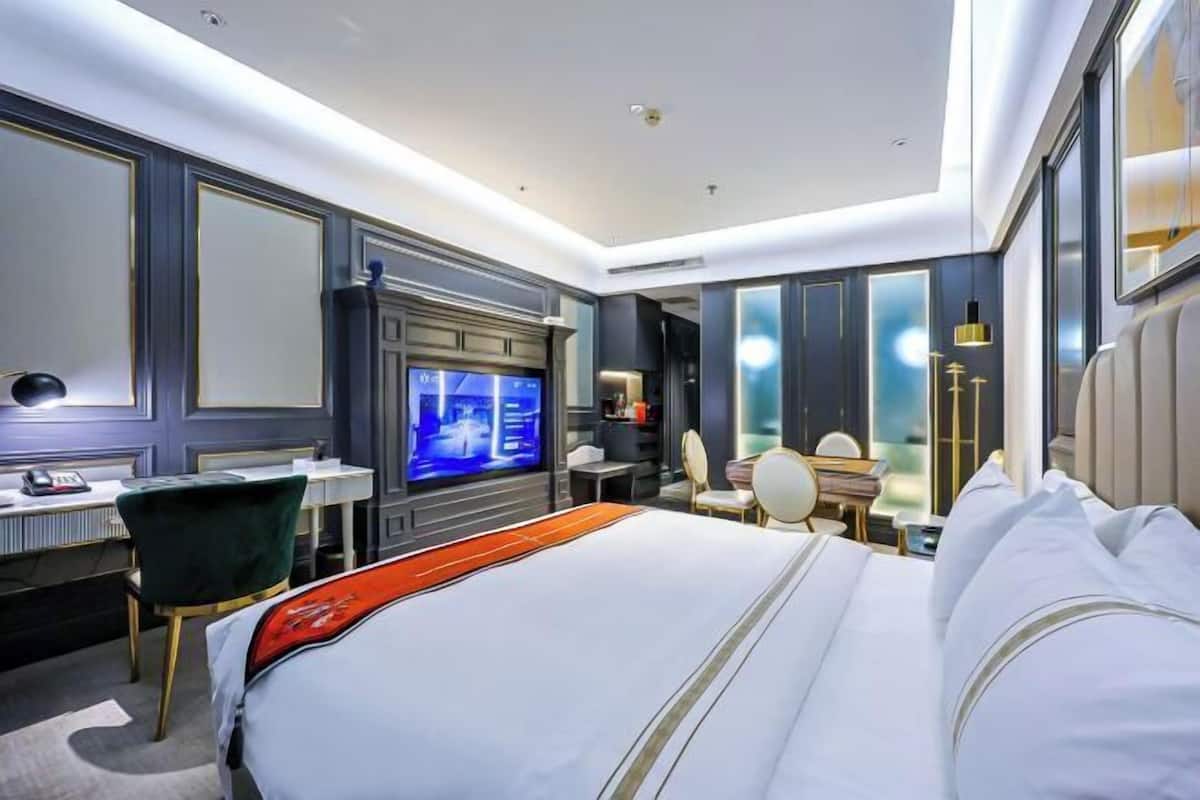 A hotel room with a large bed, a desk with a chair, a television, and a seating area with a table and chairs.