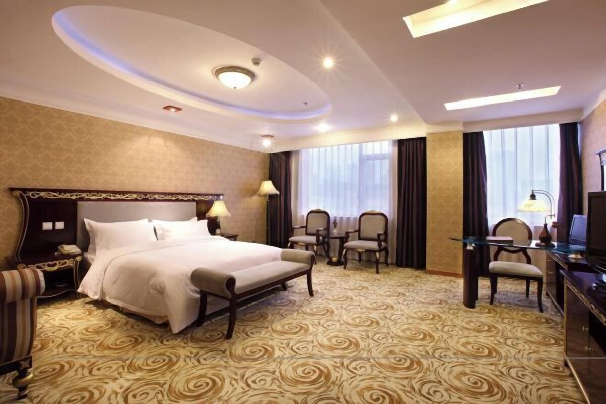Quarto de hotel com uma cama grande, uma escrivaninha com cadeira, uma televisão e uma pequena mesa com cadeiras.
