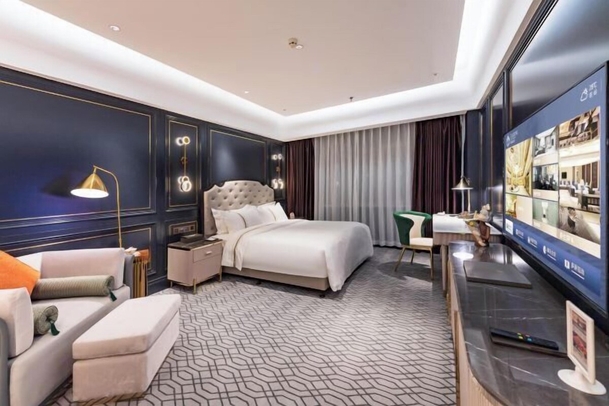 Quarto de hotel moderno com uma cama grande, uma mesa de trabalho, televisão e um espaço para sentar.