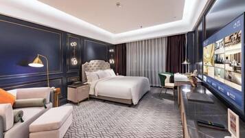 A modern hotel room with a large bed, a desk, a television, and a seating area.