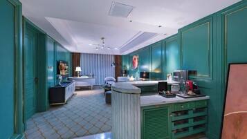 A modern hotel room with teal walls, a marble-tiled floor, a central island counter, a bed with white linens, and a large window with curtains.