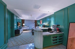 Una habitación de hotel moderna con paredes color turquesa, piso de baldosas de mármol, una encimera central tipo isla, una cama con ropa de cama blanca y un amplio ventanal con cortinas.