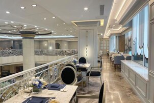 Un vestíbulo de hotel con piso de mármol, varias zonas de comedor y un balcón con barandillas.