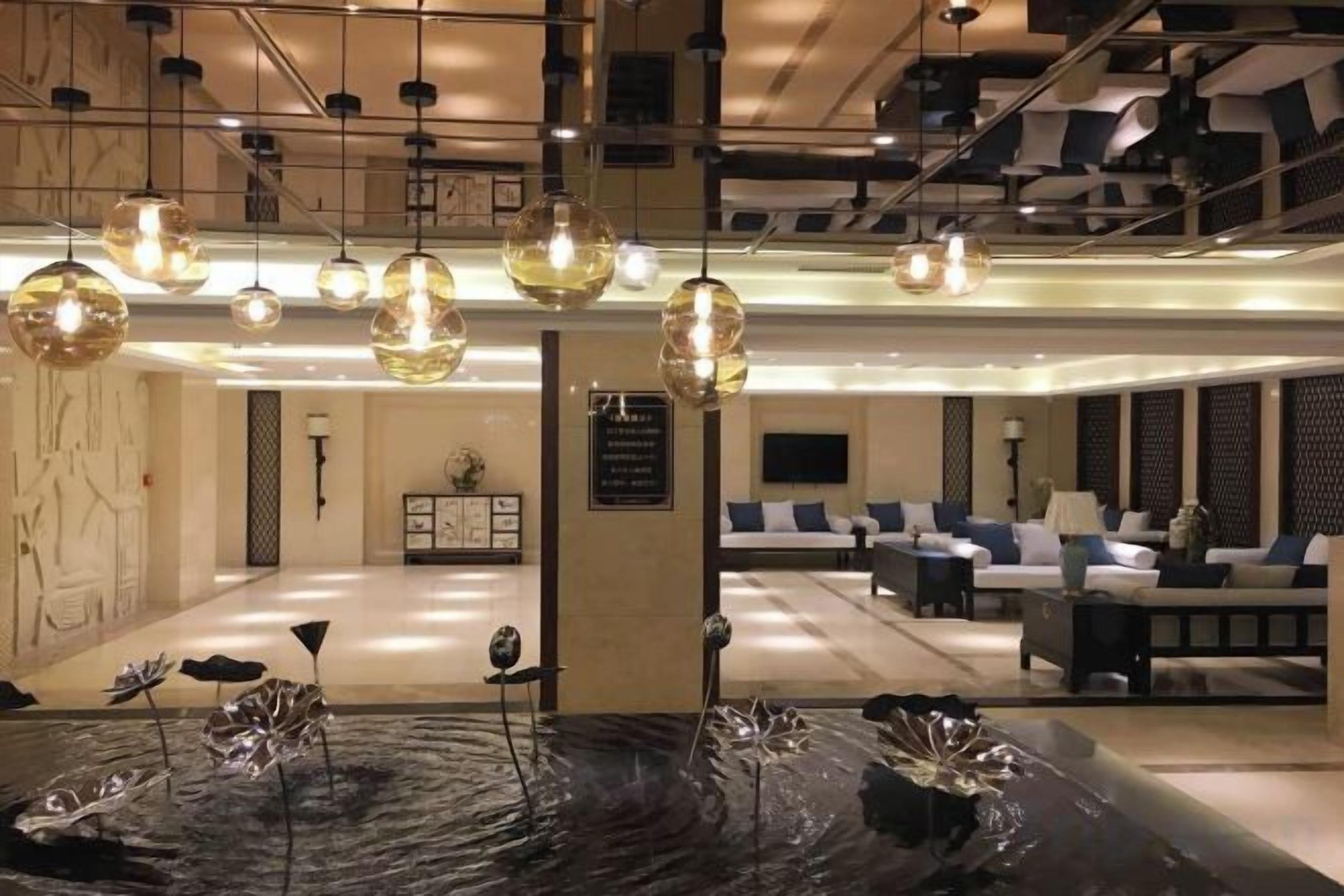 A hotel lobby with a reception desk, seating area, and decorative light fixtures.