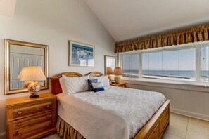 Un dormitorio con cama, dos lámparas de noche, mesita de noche, cómoda, ventana con persianas y un cuadro en la pared.