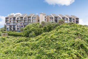Un edificio residencial de varios pisos con balcones, rodeado de abundante vegetación.