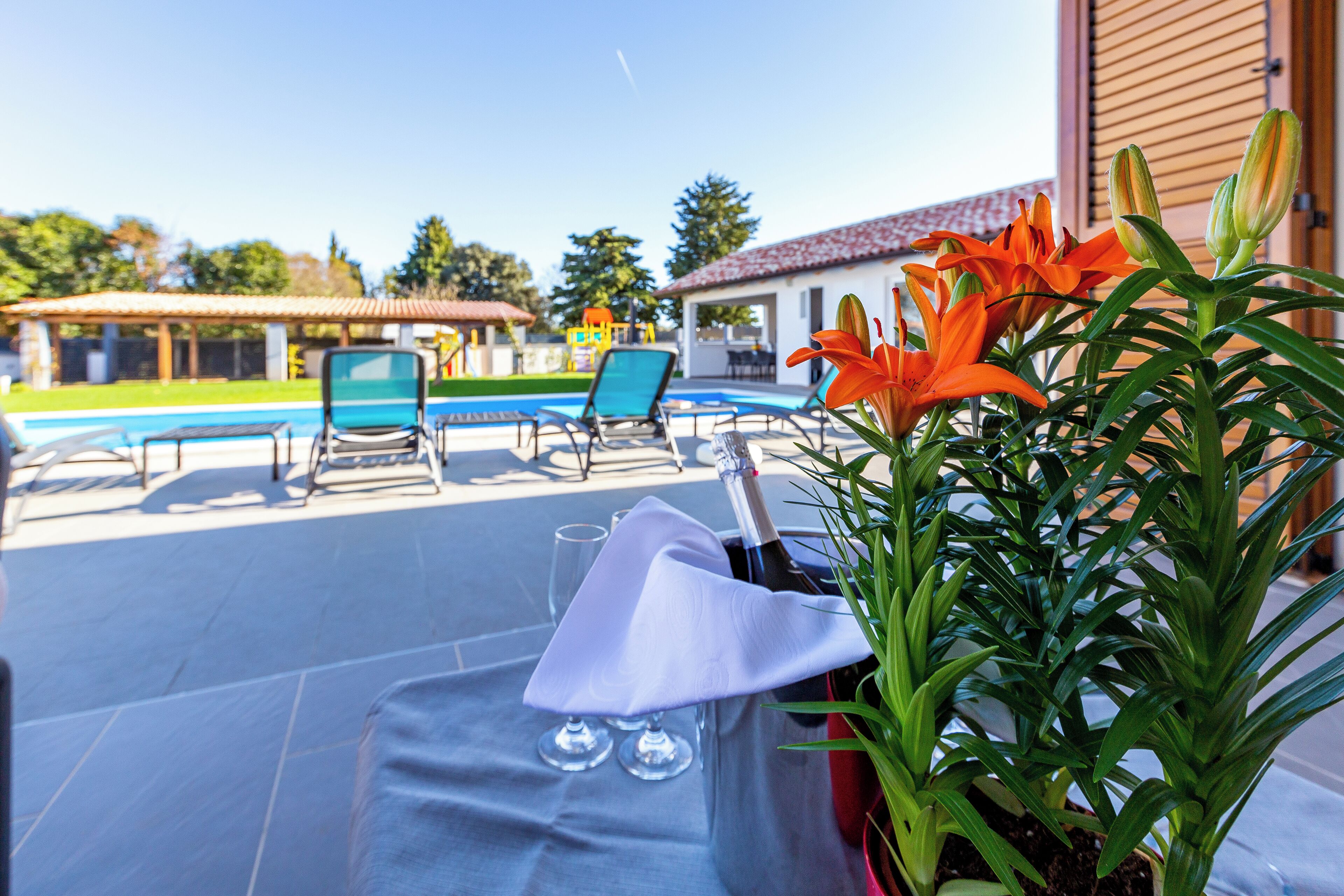 A poolside area with lounge chairs, a table with a bottle of champagne, and a potted plant.