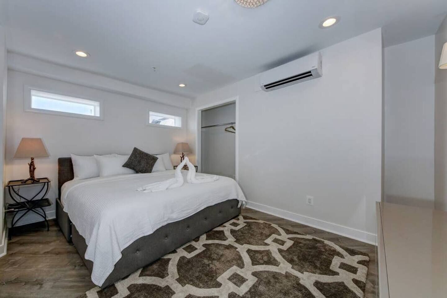 A bedroom with a bed, two bedside lamps, a rug, and an air conditioning unit.