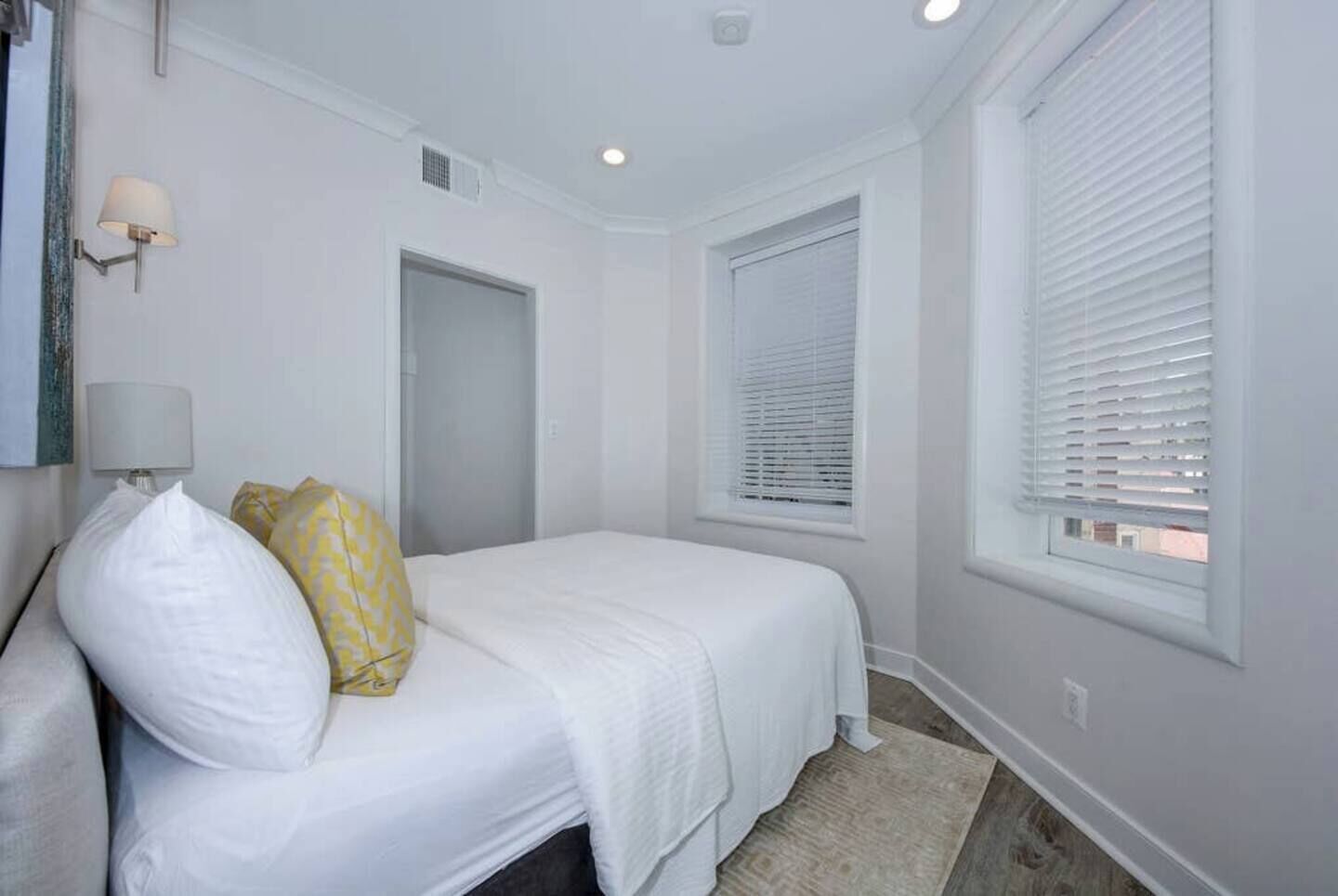A bedroom with a bed, two bedside lamps, a window with blinds, and a door.