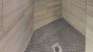 Een douche met een vloer van hexagontegels en een handdouche.