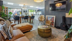 A modern living room with a sofa, coffee table, and dining area. There is a TV mounted on the wall, a guitar, and a plant. - 5 bedroom accommodation in Hove (Hove)