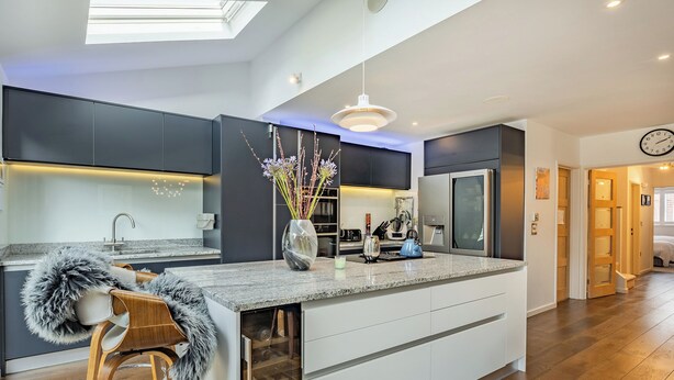 A modern kitchen with a central island, dark cabinetry, a built-in wine cooler, and a bar stool with a fur throw. - 5 bedroom accommodation in Hove (Hove)