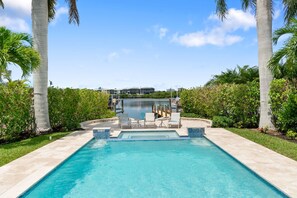 Una piscina rectangular con un elemento acuático de agua azul cristalina, rodeada por una terraza pavimentada.