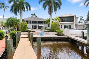 A waterfront property with a wooden dock leading to a pool area, surrounded by palm trees and modern buildings.