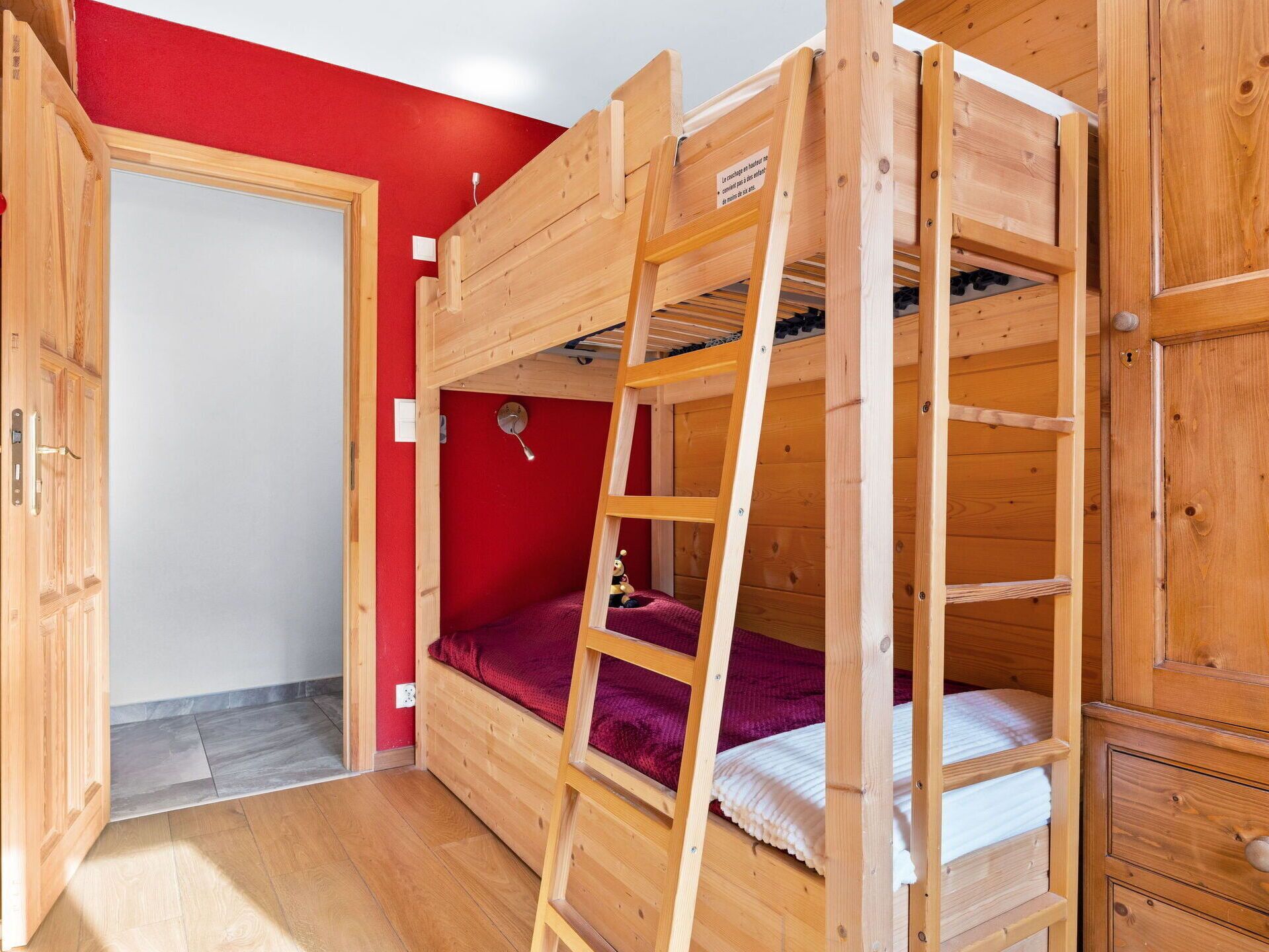 Une chambre avec un lit superposé, une échelle, un mur rouge et une porte en bois.