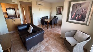A living room with a black leather sofa, a dining table with chairs, a wicker chair, a kitchen with a refrigerator, and a framed painting on the wall. - Beautiful apartment with views (Pedreguer)