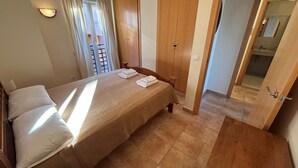 A bedroom with a bed, two pillows, a wooden wardrobe, a bathroom visible through an open door, and a balcony with curtains. - Beautiful apartment with views (Pedreguer)