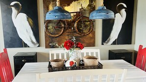 Ein Essbereich mit einem weißen Tisch, roten Stühlen, einer Vase mit roten Blumen und zwei an der Wand befestigten Fahrrädern.