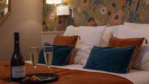 Un lit avec des oreillers blancs et bleus, une bouteille de vin et deux verres de vin sur un plateau.