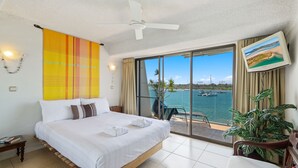 Hotelkamer met een groot bed, een plafondventilator, uitzicht op zee en een aan de muur bevestigde televisie.