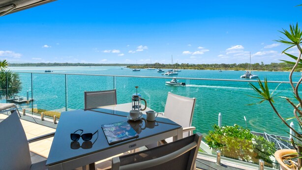 Een balkon met een tafel gedekt voor twee personen, met uitzicht op een jachthaven vol boten en een helderblauwe lucht.