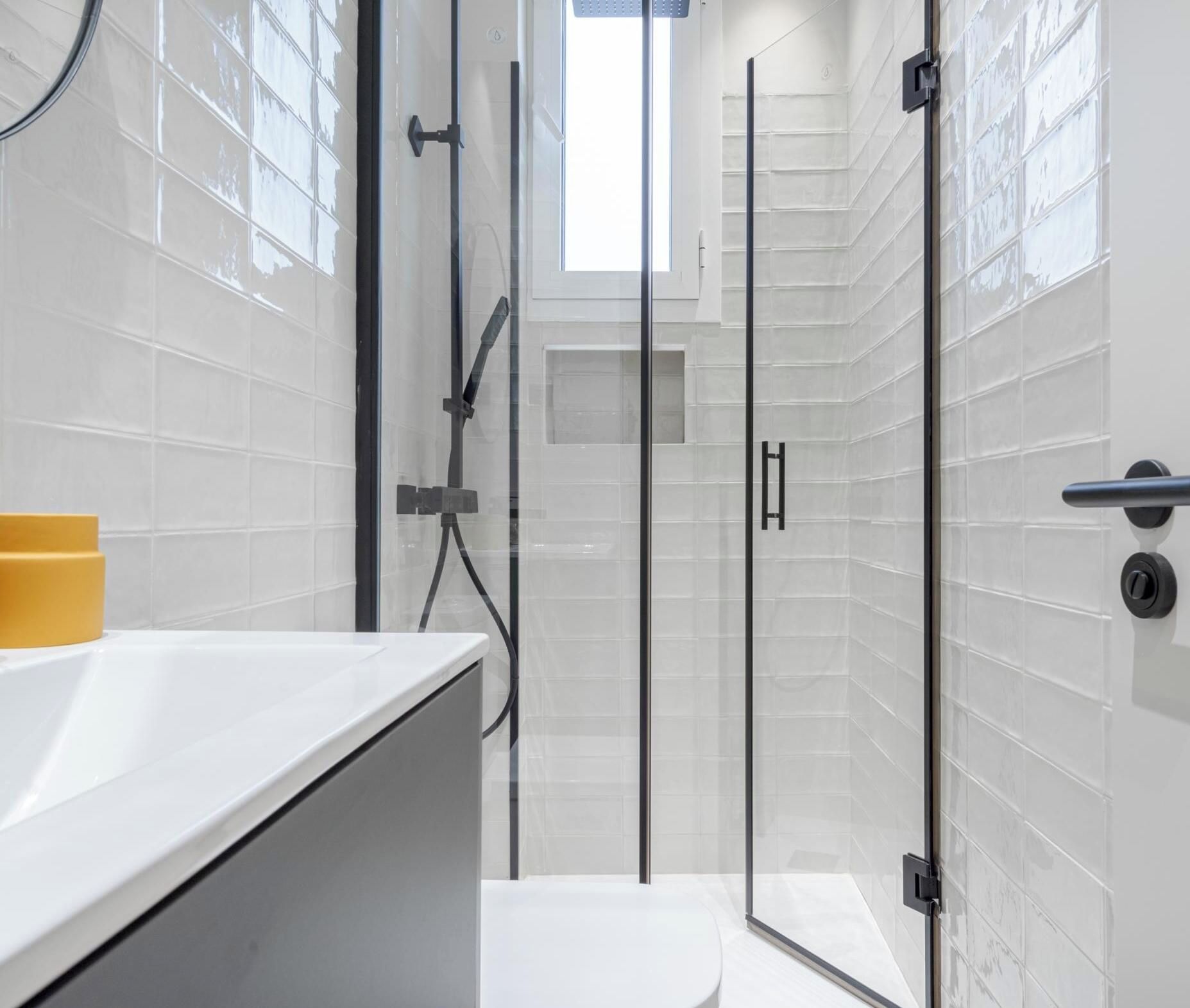 Un baño moderno con cabina de ducha de vidrio, un lavabo blanco y un jabonera amarilla.