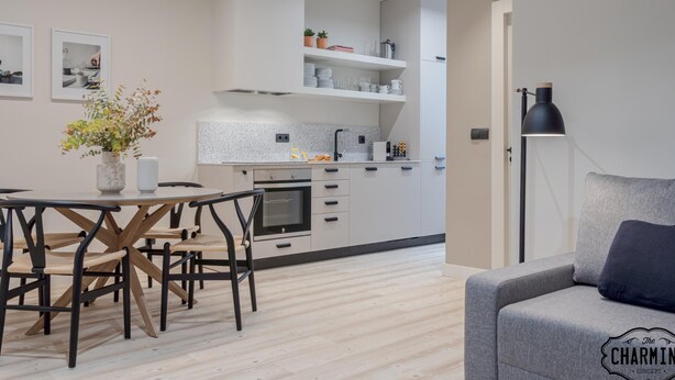 A modern kitchen with white cabinets, a dining table with chairs, and a grey sofa. - Retiro Chic - One-bedroom Apartment (Madrid)