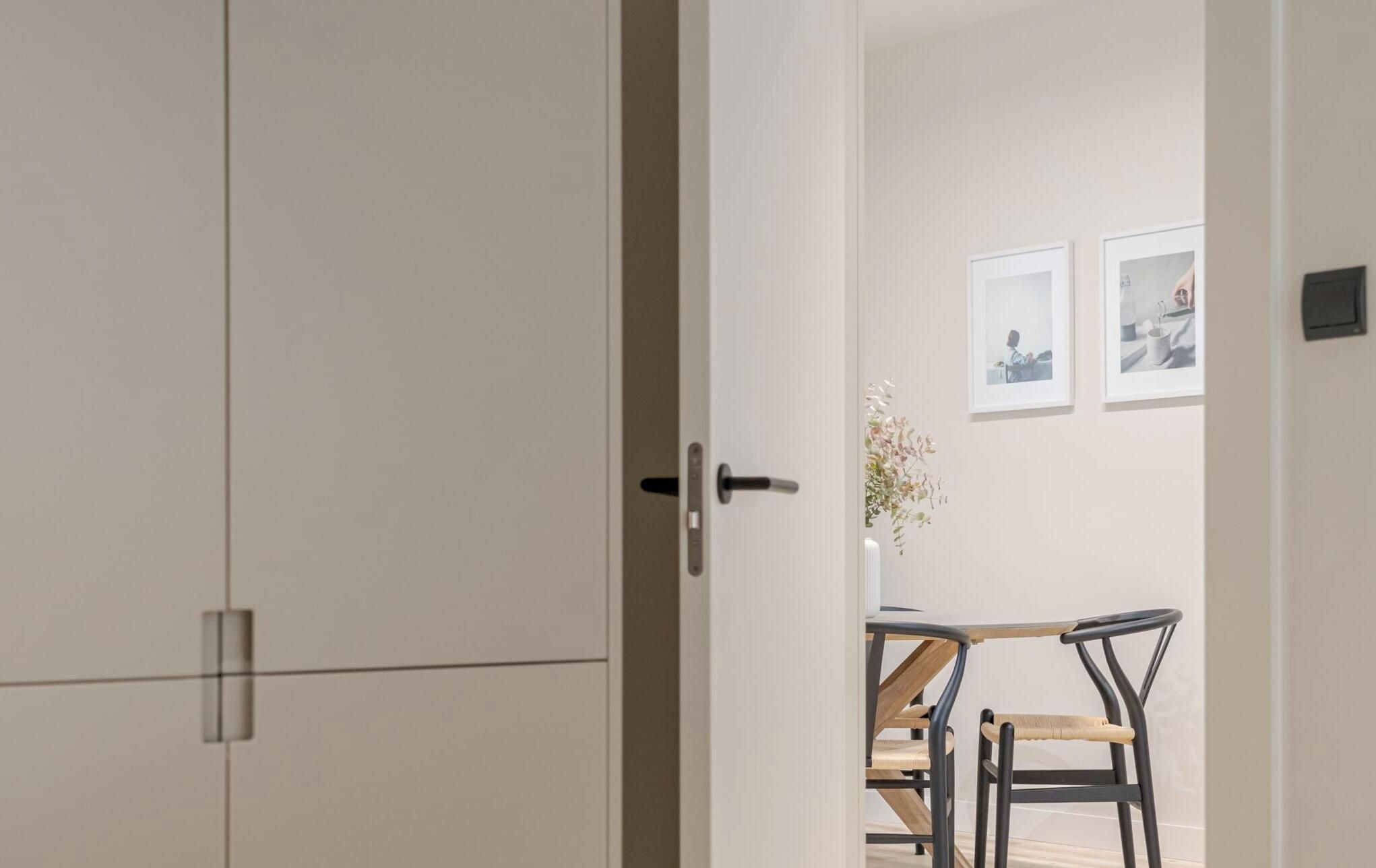Una habitación con la puerta cerrada, una mesa de comedor con sillas y cuadros en la pared.