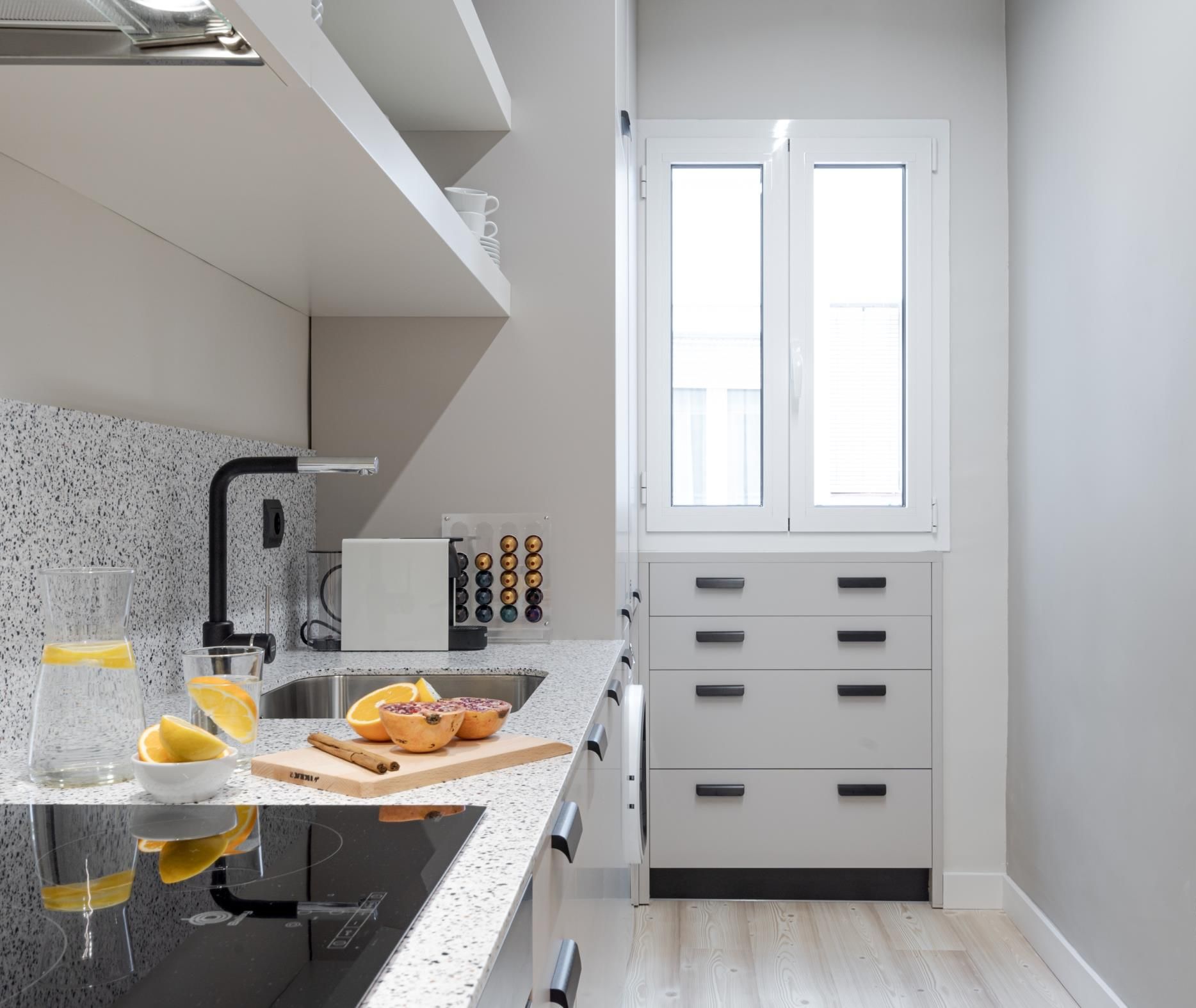 A modern kitchen with a granite countertop, a built-in oven, and a window with blinds.