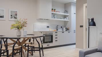 Una cocina moderna con armarios blancos, una mesa de comedor con sillas y un sofá gris.