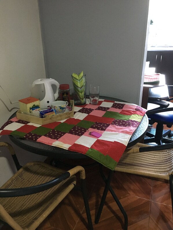 A dining area with a table covered by a patchwork tablecloth, surrounded by wicker chairs.