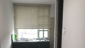 A narrow hallway with a kitchen area featuring a window with blinds, a sink, and cabinets. - ENCANTO CERCA DEL AEROPUERTO - APARTAESTUDIO PEQUEÑO (Bogota)