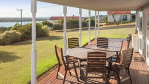 A covered outdoor patio with a wooden table and chairs, overlooking a grassy area and a body of water.