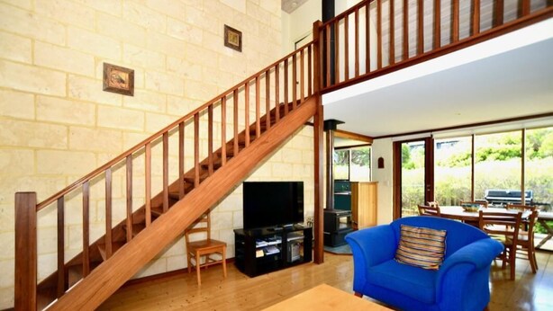 Una sala de estar con una escalera de madera, un sofá azul, una mesa de centro de madera y un televisor.