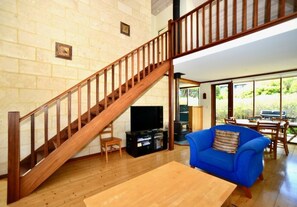 A living room with a wooden staircase, a blue sofa, a wooden coffee table, and a television. - Cowrie Chalet - close to the river and town - Cowrie Chalet - Close to the river (Augusta)