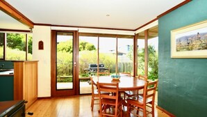 Un comedor con una mesa redonda y sillas, una zona de cocina con estufa, y una puerta corrediza de vidrio que da a un patio exterior con una parrilla.