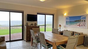 A dining area with a view of the sea, a television, and a beach scene painting.