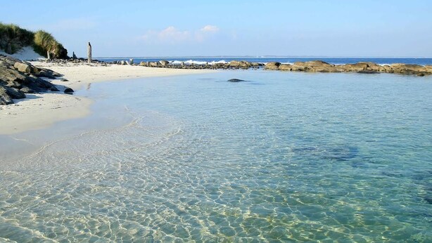 A beach with clear shallow waters, a sandy shore, and rocky outcrops.